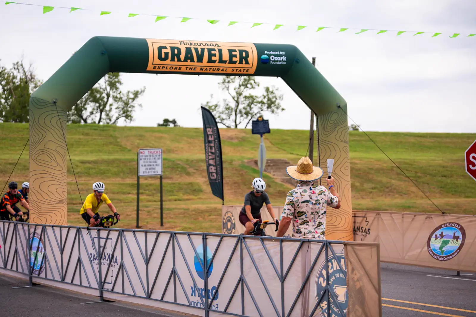Riders rolling under the Arkansas Graveler finish arch as a volunteer rings a cowbell