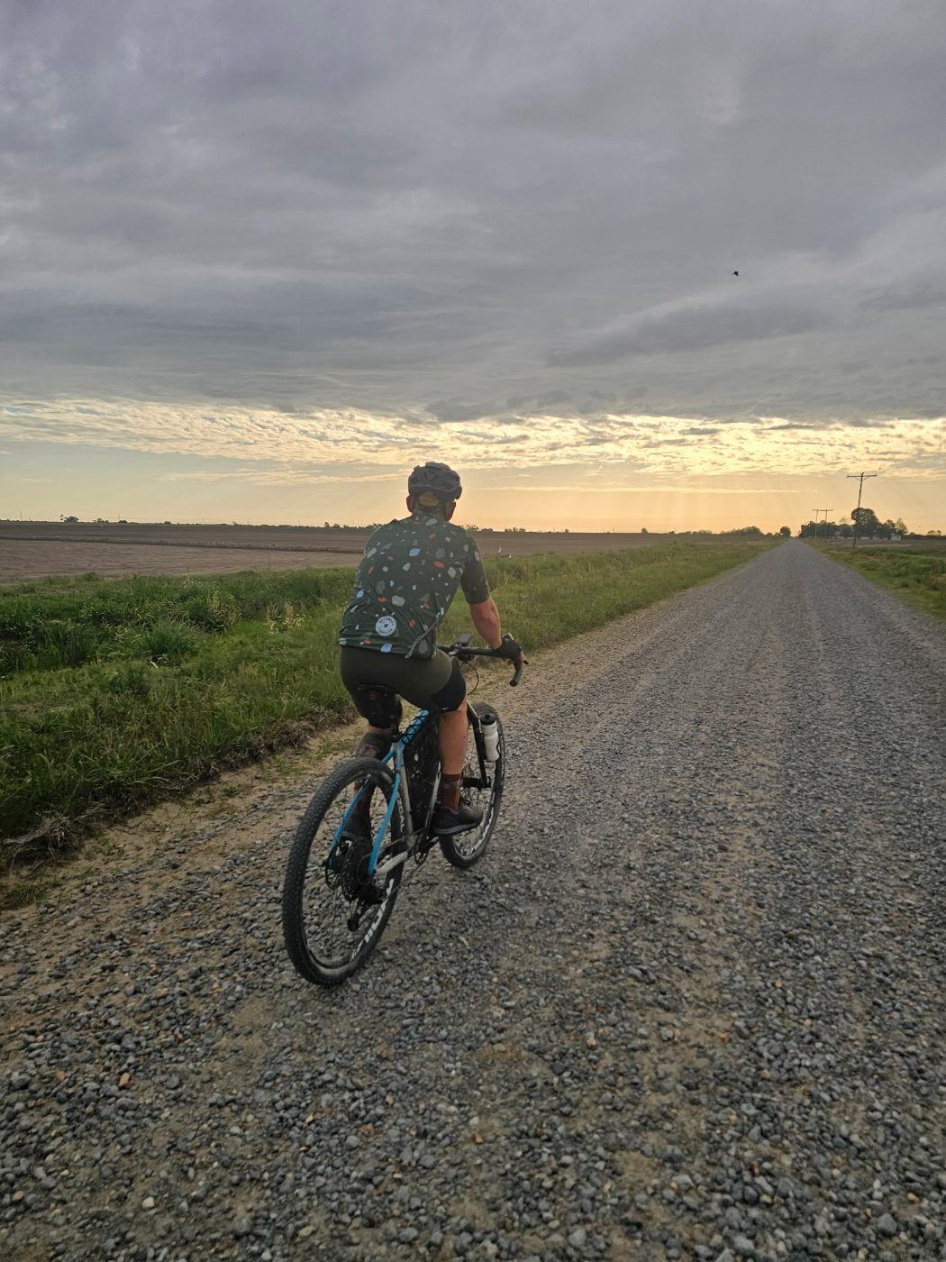 A rider on a gravel road running flat to the horizon at sunrise