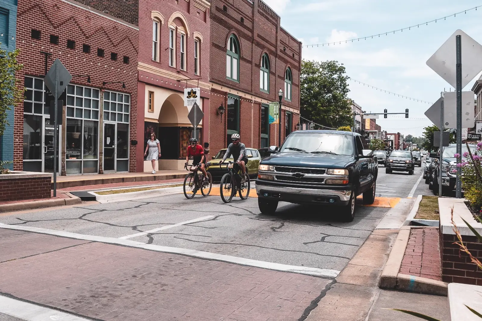 Two Arkansas Graveler cyclists riding past storefronts on a Delta town main street