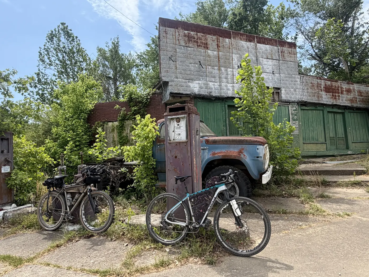Two gravel bikes parked at the old gas pumps of a weathered rural store
